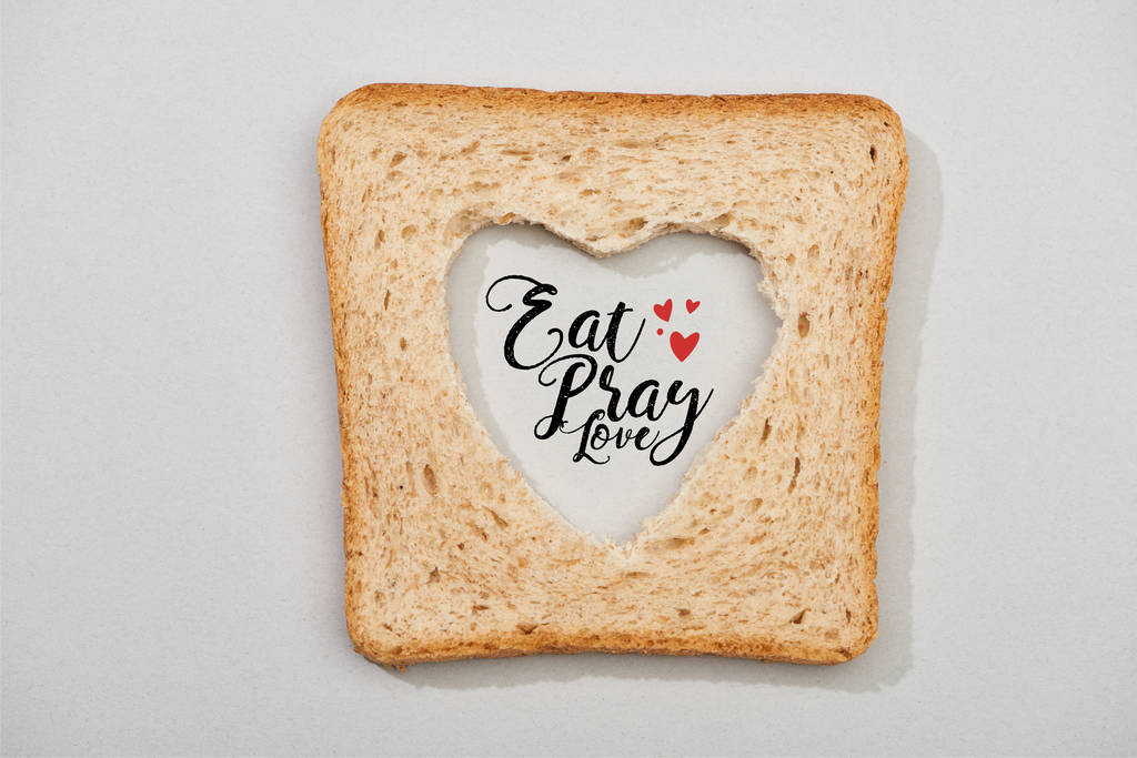 Вид зверху на шматочок хліба з різьбленим серцем і їсти, молитись, кохати малювання на сірому фоні
 - Фото, зображення