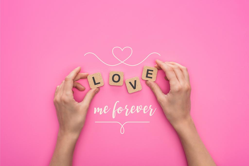 Teilansicht einer Frau, die Würfel mit Love me forever Schriftzug auf rosa Hintergrund hält - Foto, Bild
