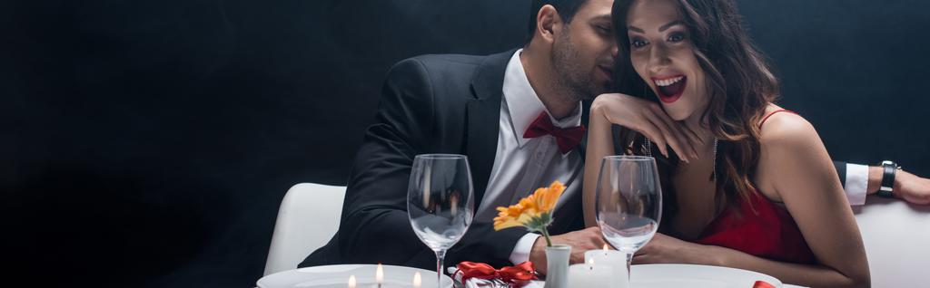 Plan panoramique d'un bel homme chuchotant à une femme choquée lors d'un dîner romantique isolé sur noir
 - Photo, image