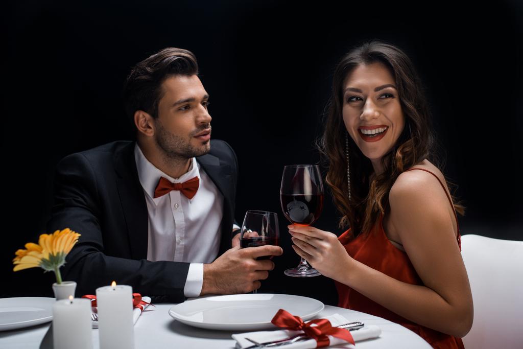 Przystojny mężczyzna patrzy na uśmiechniętą kobietę podczas romantycznej kolacji odizolowaną na czarno - Zdjęcie, obraz