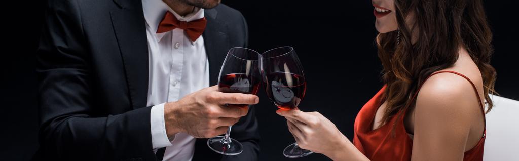 Panoramic shot of elegance couple clinking with wine glasses isolated on black - Photo, Image
