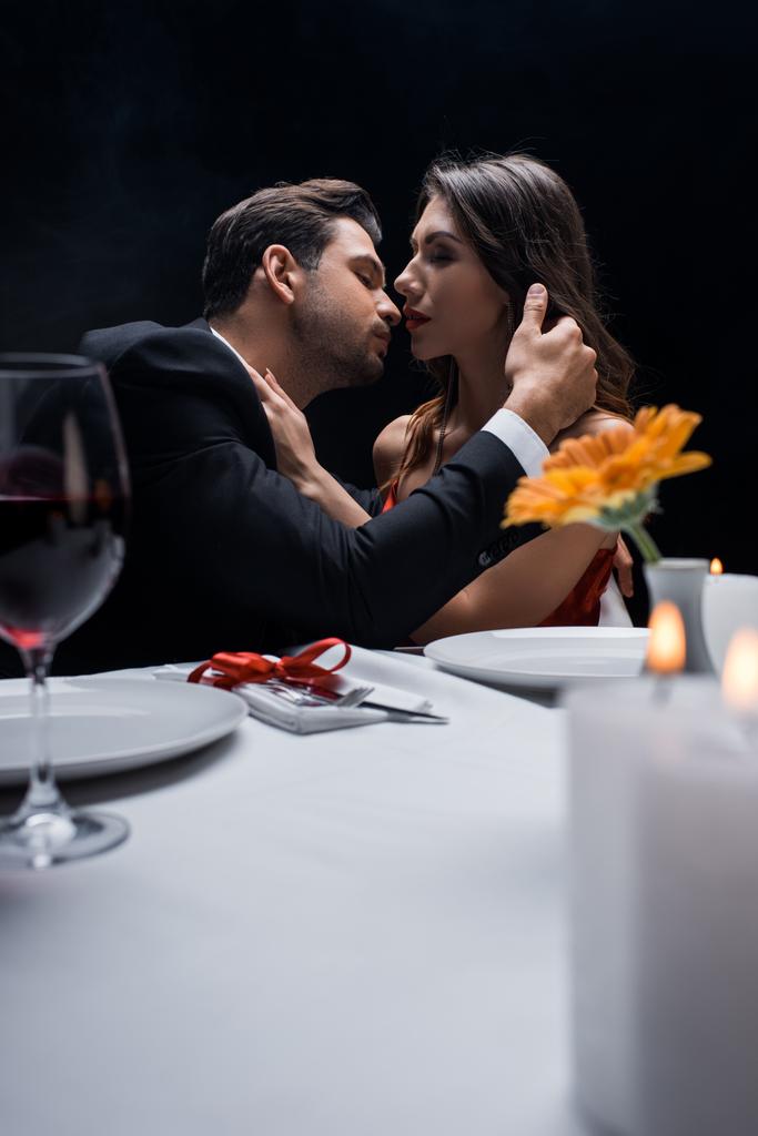 Selectieve focus van elegant koppel kussen tijdens romantisch diner geïsoleerd op zwart - Foto, afbeelding