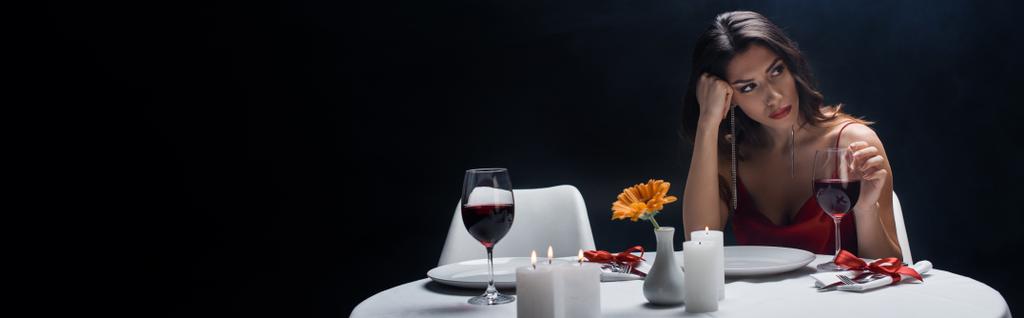 Vue panoramique de femme ennuyeuse regardant loin de la table servie isolé sur noir
 - Photo, image