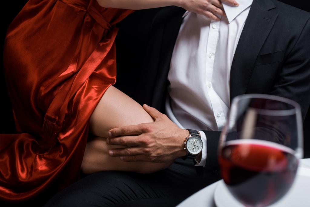 abgeschnittene Ansicht eines Mannes, der eine elegante Frau am Knie hält, während eines romantischen Abendessens isoliert auf schwarz - Foto, Bild