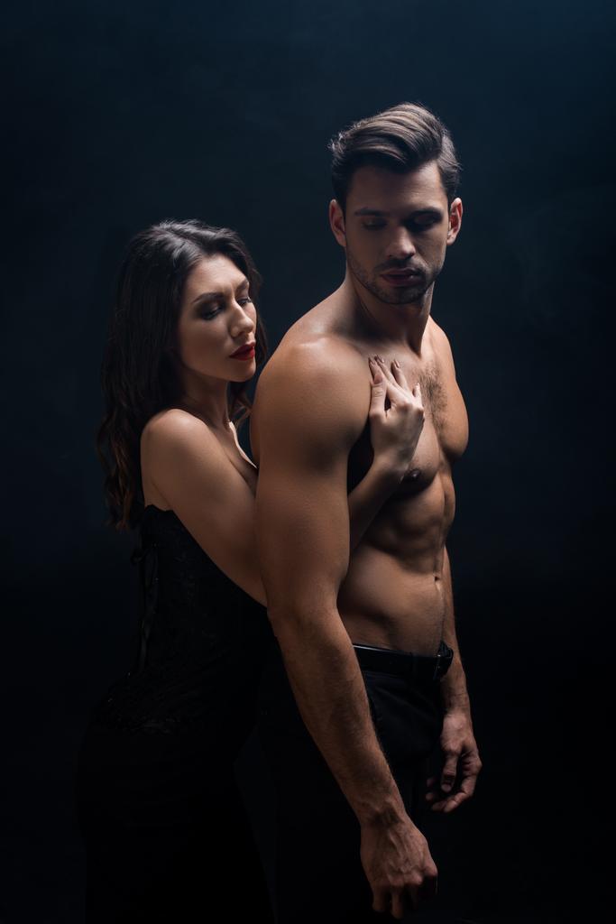 Side view of attractive girl touching shirtless man isolated on black - Photo, Image