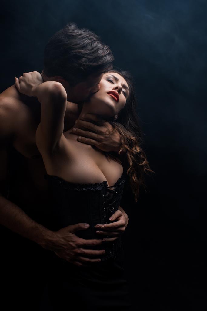 Félmeztelen férfi csók és ölelés érzéki nő fűzőben elszigetelt fekete - Fotó, kép