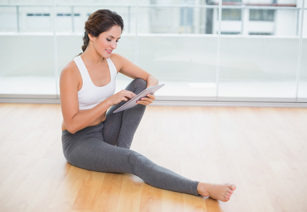 sportowy szczęśliwy brunetka za pomocą tabletu, siedząc na podłodze - Zdjęcie, obraz