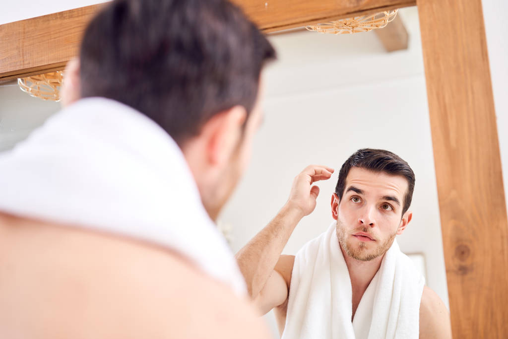 Jovem macho com toalha branca no pescoço em pé perto do espelho
 - Foto, Imagem