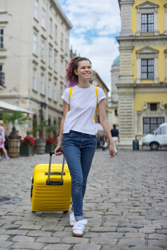 Meisje tiener wandelen met rugzak en gele koffer op straat - Foto, afbeelding