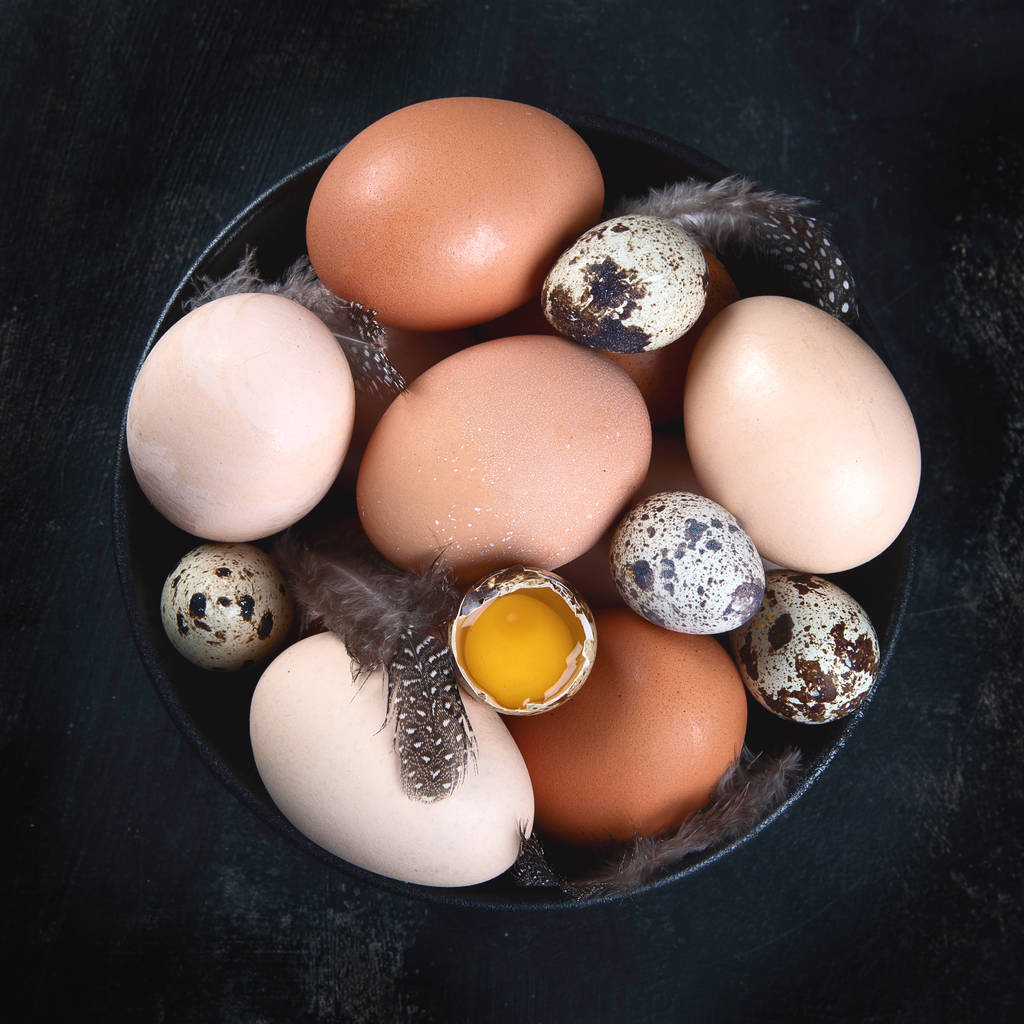 Różne rodzaje świeżych jaj w misce na czarnym tle. Produkty rolne. Widok z góry, płaski leżak z przestrzenią do kopiowania - Zdjęcie, obraz