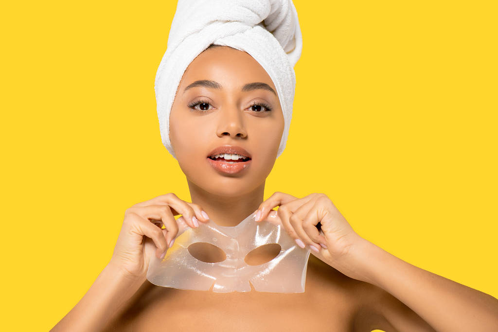 african american girl with towel on head holding hydrogel mask, isolated on yellow - 写真・画像