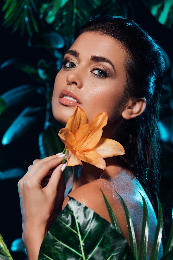 Genç ve güzel bir kadın yeşil yaprakların yanında orkide tutuyor.  - Fotoğraf, Görsel