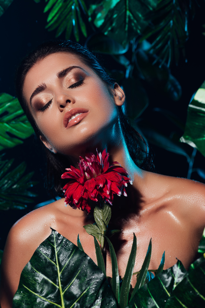 young sexy woman holding red blooming flower near green leaves  - Photo, Image
