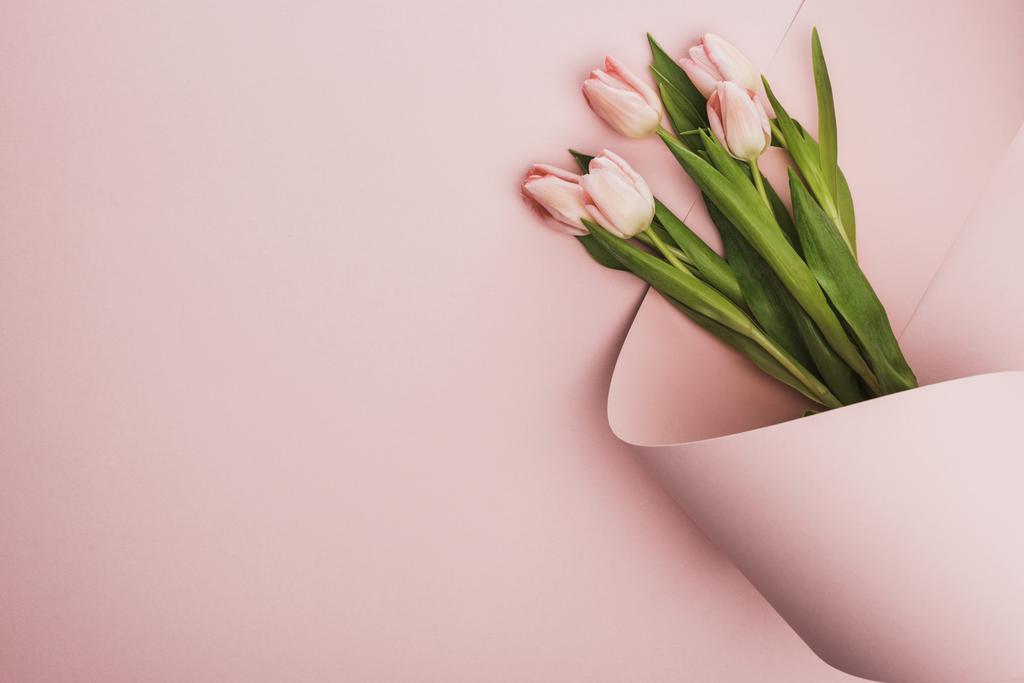 horní pohled na tulipán kytice zabalené v papírové víření na růžovém pozadí - Fotografie, Obrázek