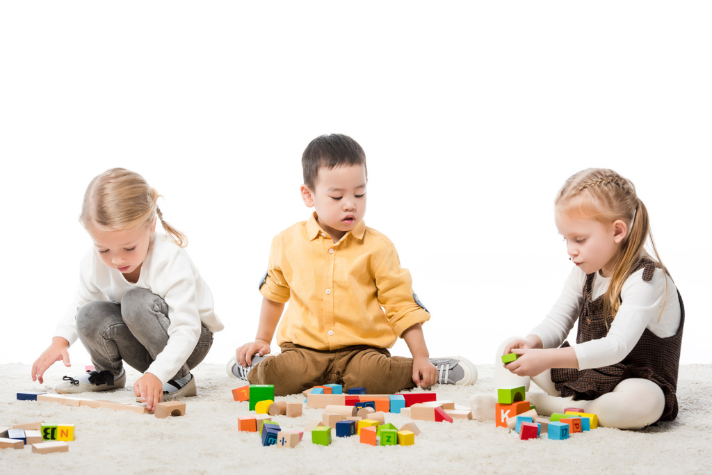 multiethnische Kinder, die mit Holzklötzen auf Teppich spielen, isoliert auf Weiß - Foto, Bild