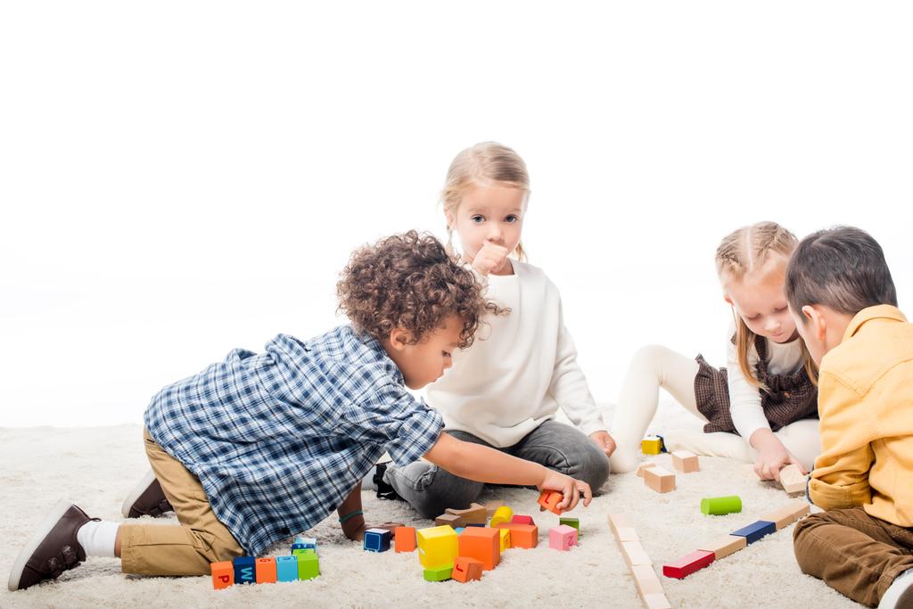 multicultural kids playing with wooden blocks on carpet, isolated on white - Photo, Image