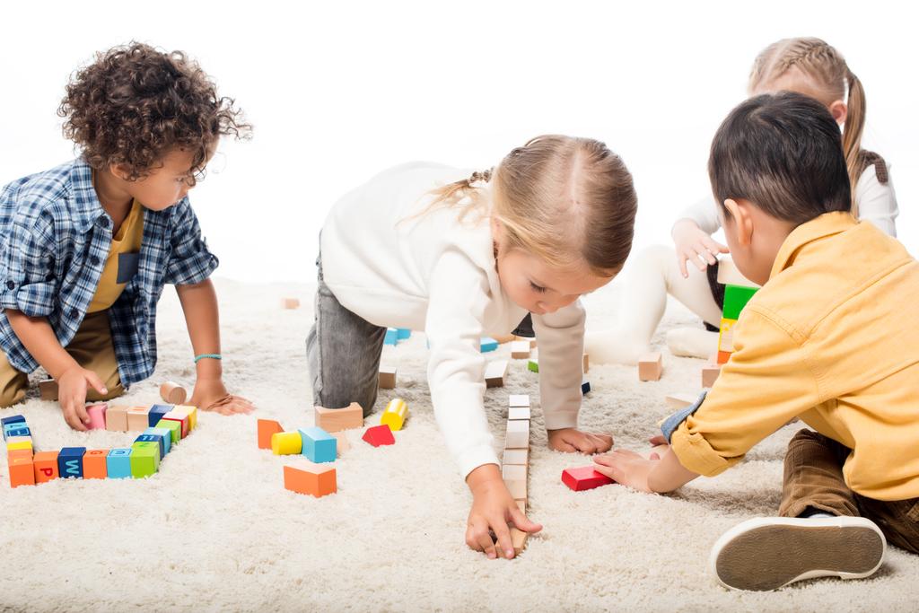 crianças multiétnicas brincando com blocos de madeira no tapete, isolado em branco
 - Foto, Imagem