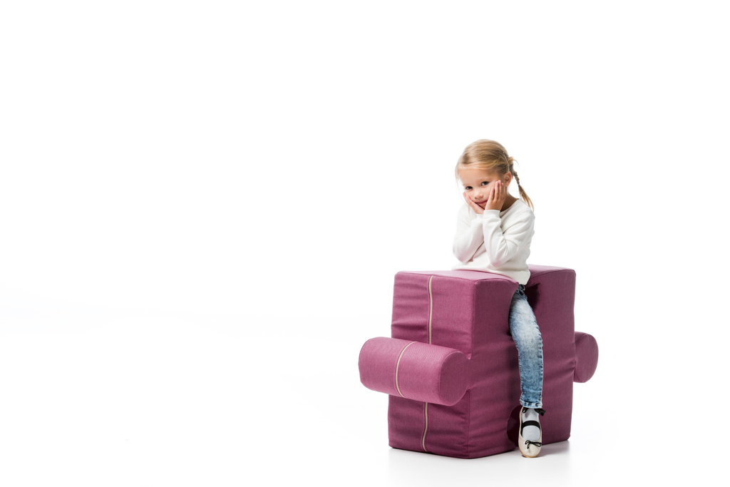 pensive kind zittend op paarse puzzel stoel, geïsoleerd op wit  - Foto, afbeelding