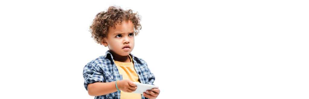 panoramiczne ujęcie małego wściekłego afrykańskiego chłopca używającego smartfona, odizolowanego na biało - Zdjęcie, obraz