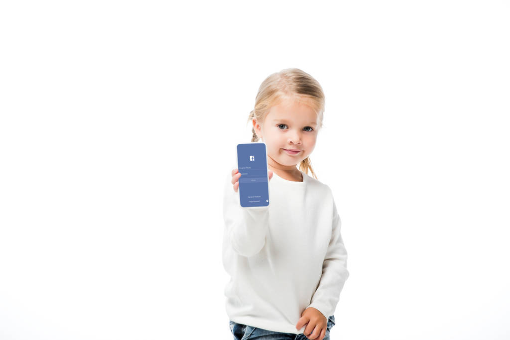 KYIV, UCRANIA - 18 de noviembre de 2019: niño adorable mostrando teléfono inteligente con aplicación de Facebook en la pantalla, aislado en blanco
 - Foto, imagen