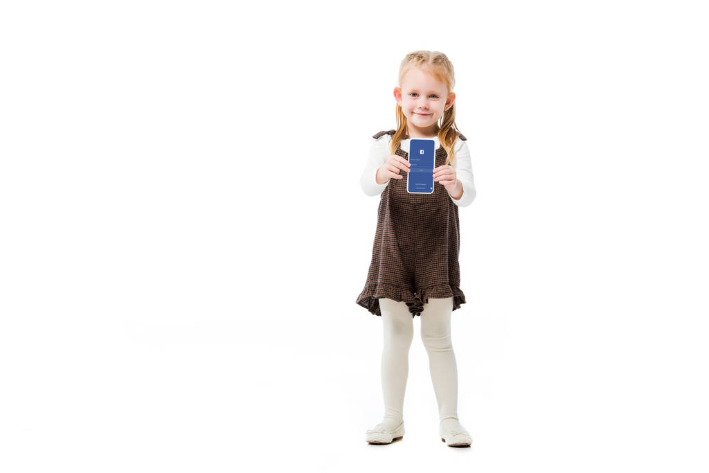 KYIV, UCRANIA - 18 de noviembre de 2019: niño adorable mostrando teléfono inteligente con aplicación de Facebook en la pantalla, aislado en blanco
 - Foto, Imagen