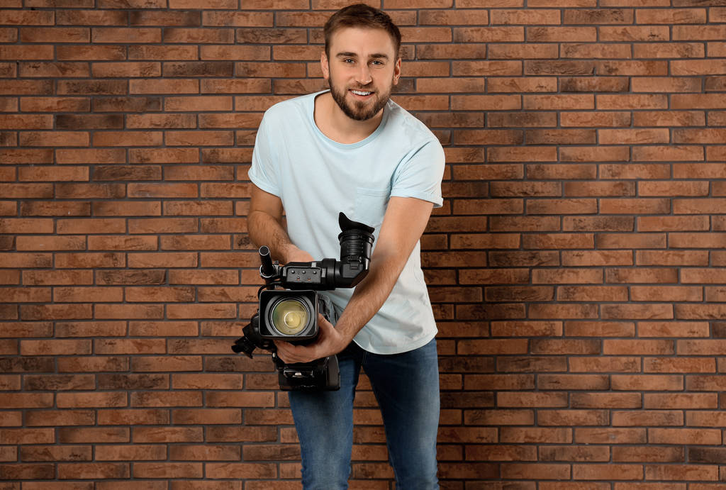 Operador com câmera de vídeo profissional perto da parede de tijolo
 - Foto, Imagem