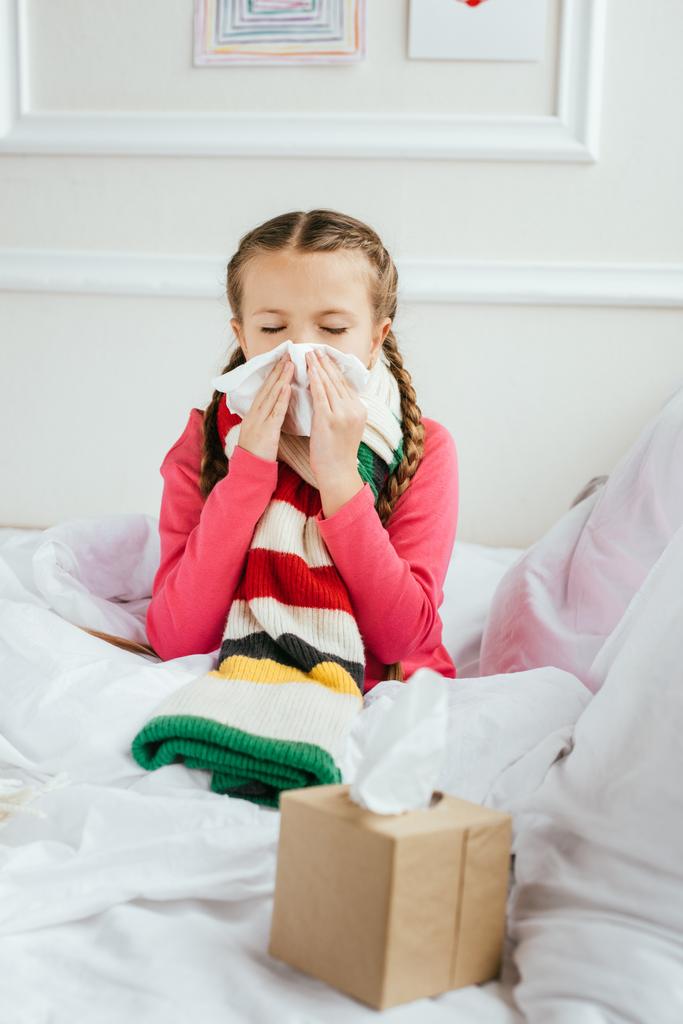 sick kid with runny nose holding napkins while sitting on bed - Photo, Image