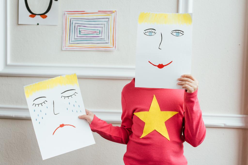 παιδί κρατώντας δύο πίνακες με χαρούμενα και λυπημένα πρόσωπα - Φωτογραφία, εικόνα