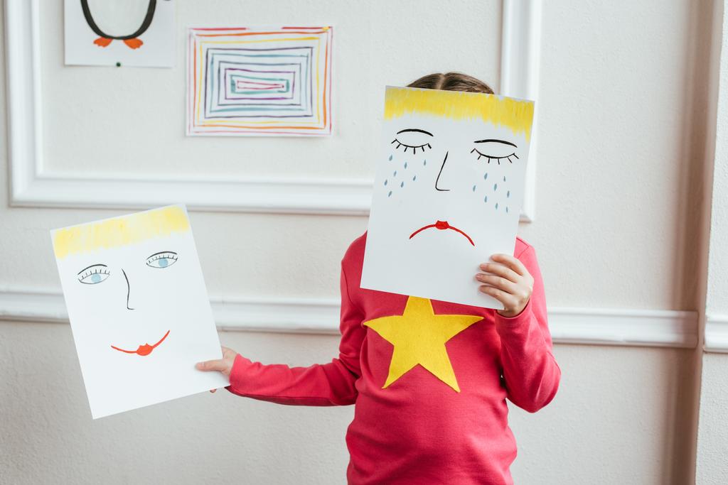 bambino in possesso di due dipinti con volti felici e tristi
 - Foto, immagini