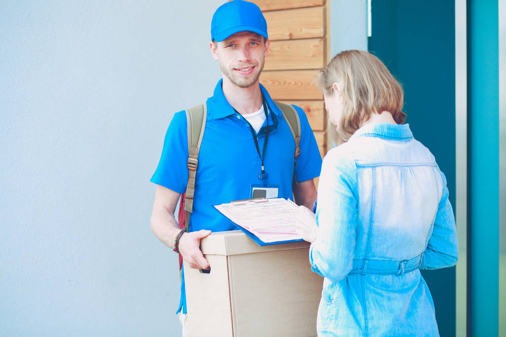 Mavi üniformalı gülümseyen kurye servis konseptine paket kutusu teslim eden teslimatçı. Mavi üniformalı gülümseyen teslimatçı. - Fotoğraf, Görsel