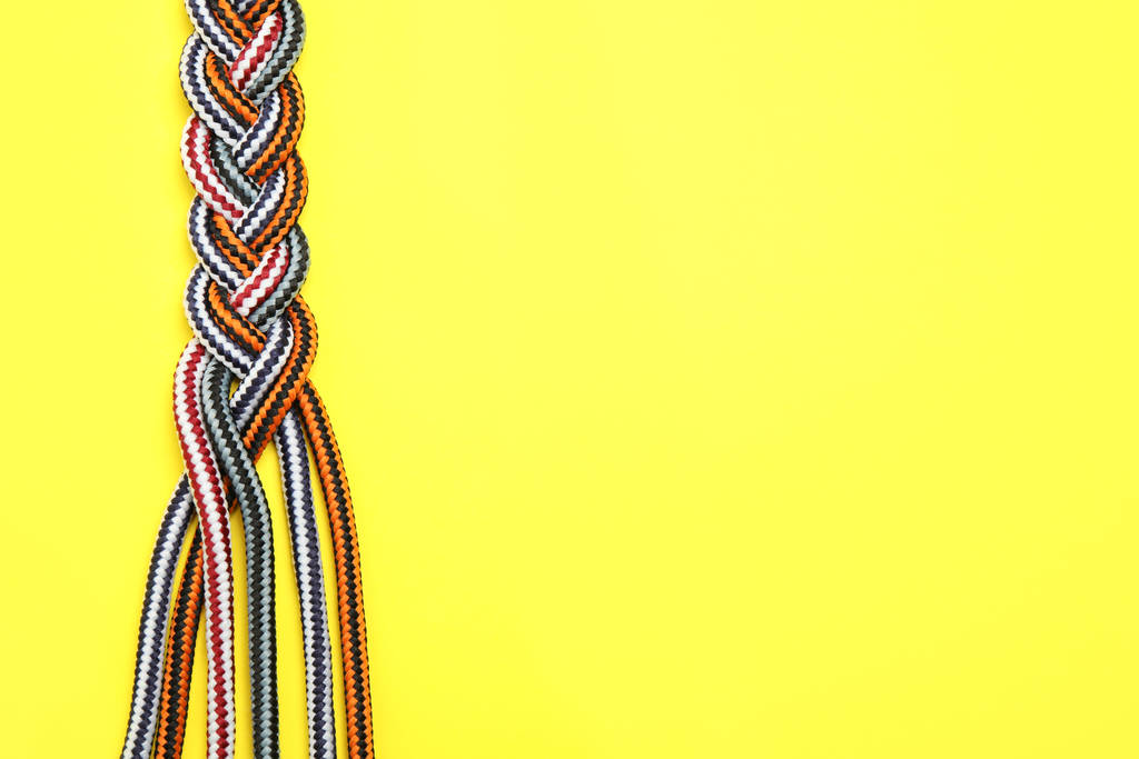 Top view of braided colorful ropes on yellow background, space for text. Unity concept - Photo, Image