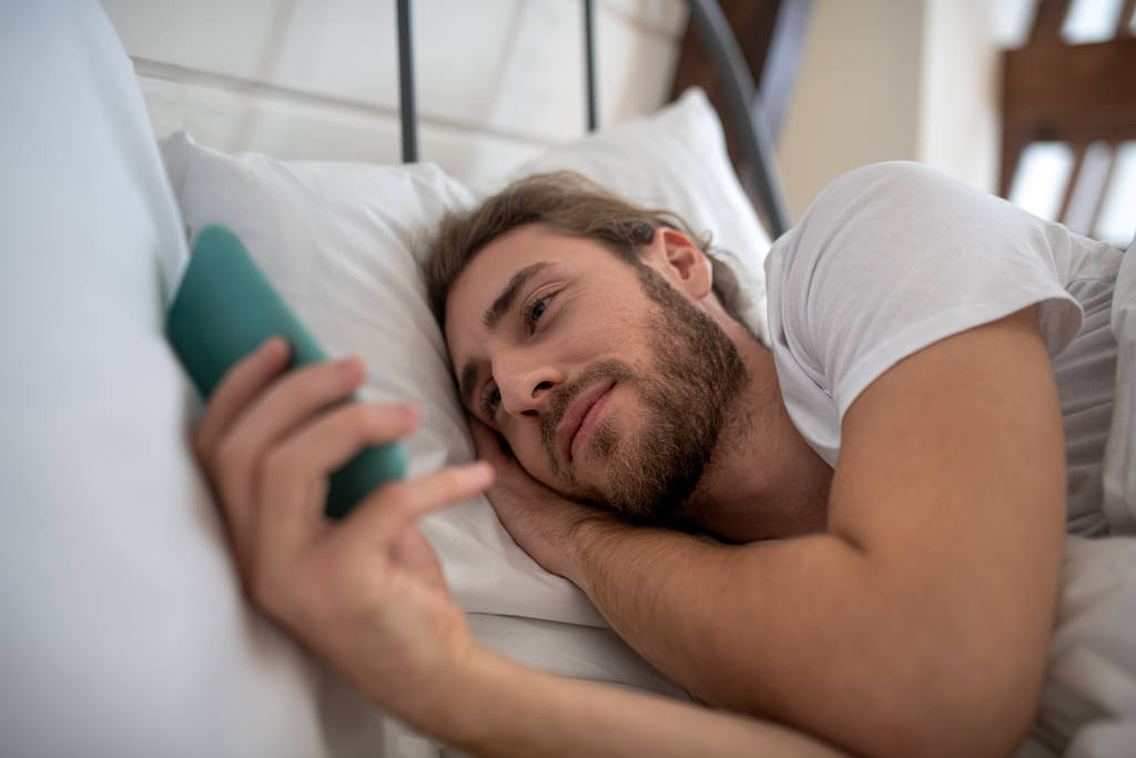 Uomo assonnato che usa il telefono nel letto
 - Foto, immagini