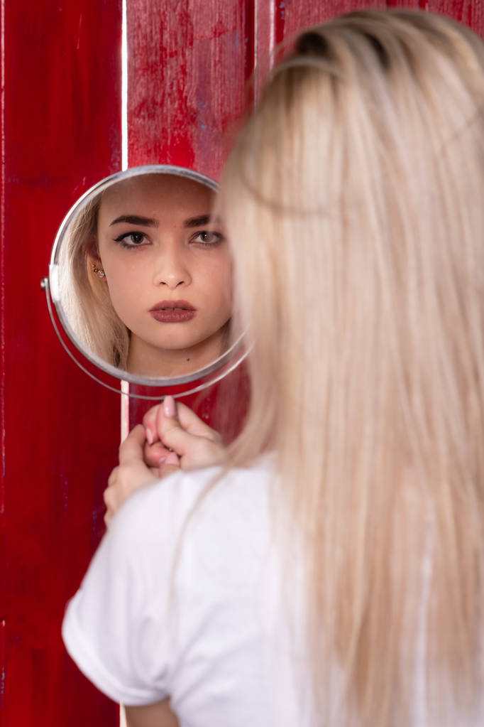 schönes junges Mädchen, das in einen runden Spiegel schaut. eine attraktive Blondine hält einen Spiegel in ihren Händen. - Foto, Bild