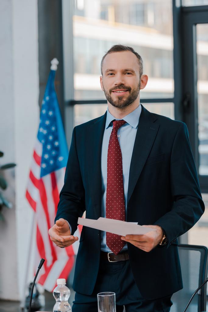 selective focus of happy diplomat in suit holding papers near american flag  - Photo, Image