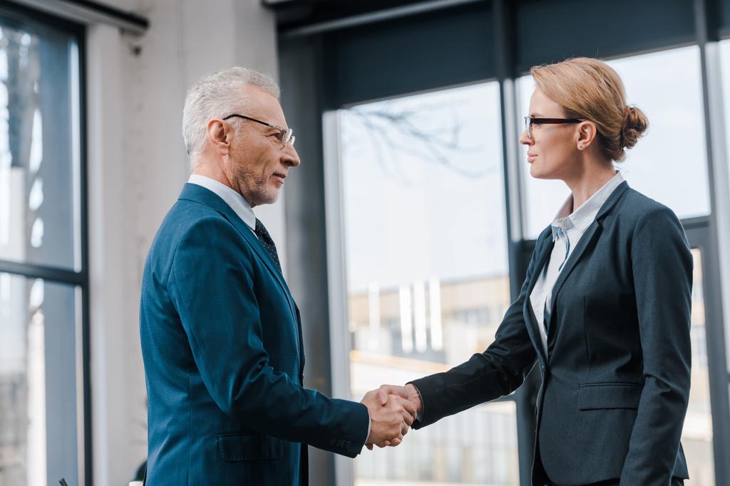 side view of businesswoman shaking hands with businessman in glasses  - Photo, Image