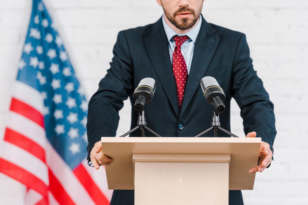 cropped view of bearded speaker in suit standing near microphones  - Photo, Image