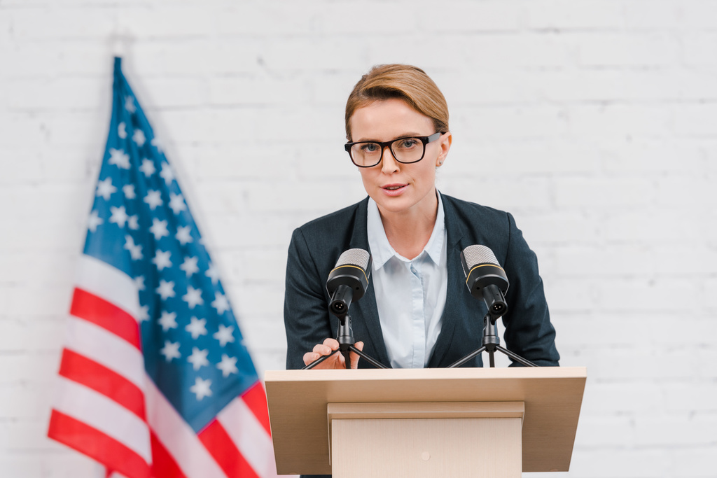 atractivo altavoz en gafas hablando cerca de micrófonos y bandera americana
  - Foto, imagen