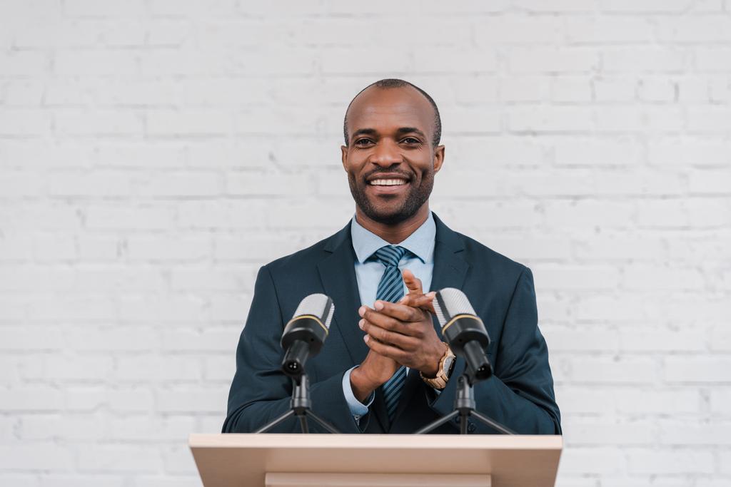 χαρούμενος αφρικάνικος αμερικανός ομιλητής χειροκροτεί κοντά στα μικρόφωνα  - Φωτογραφία, εικόνα