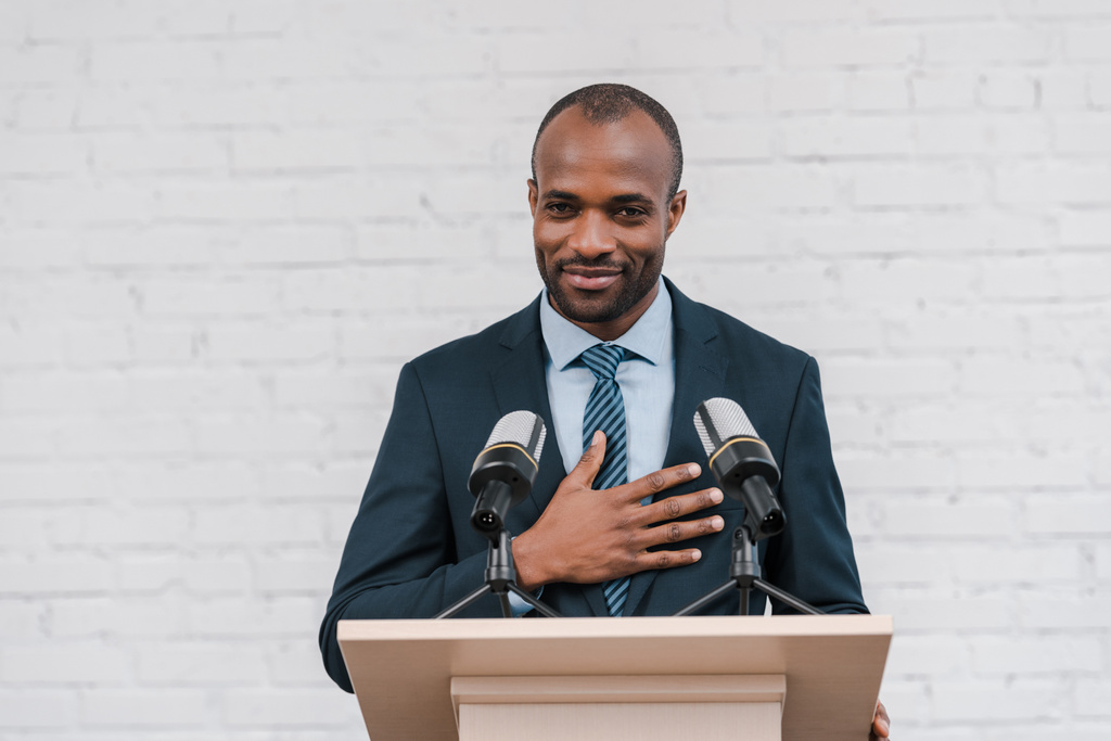 alegre afro-americano orador sorrindo perto de microfones
  - Foto, Imagem
