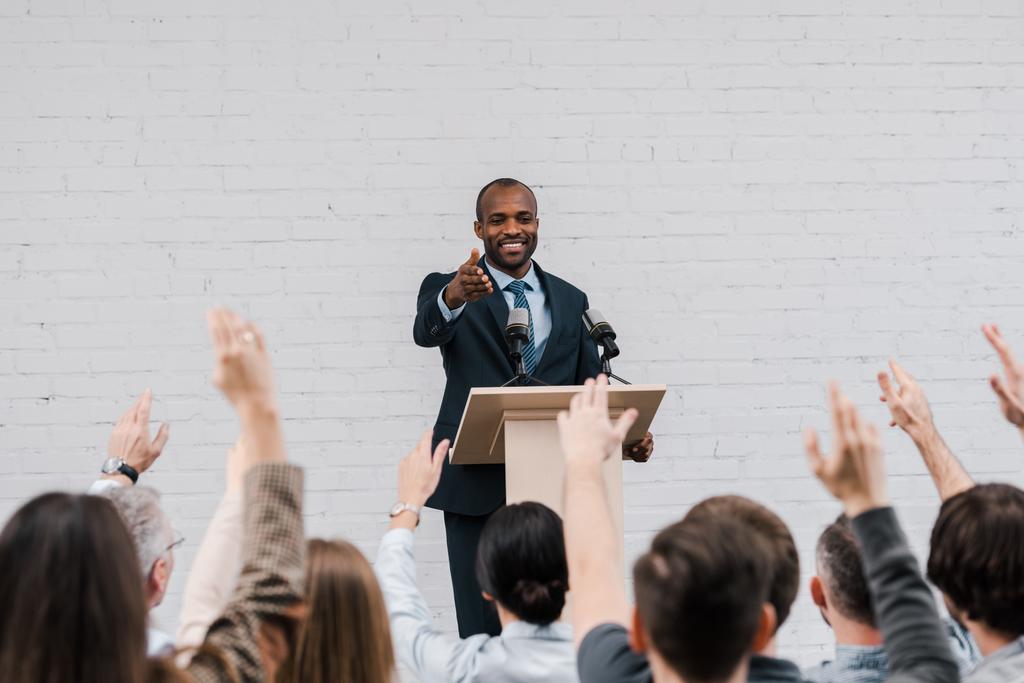 πίσω όψη των δημοσιογράφων με υψωμένα τα χέρια κοντά ευτυχής αφρικανός Αμερικανός ομιλητής gesturing κοντά σε μικρόφωνα  - Φωτογραφία, εικόνα