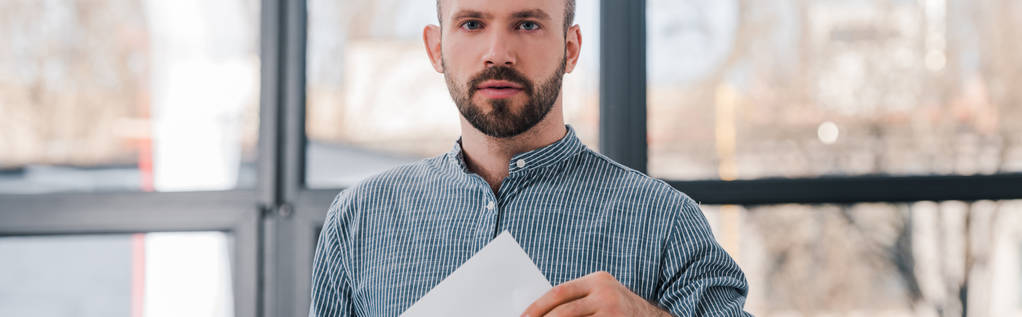 Panoramaaufnahme eines gutaussehenden Wählers mit leerem Stimmzettel und Blick in die Kamera  - Foto, Bild
