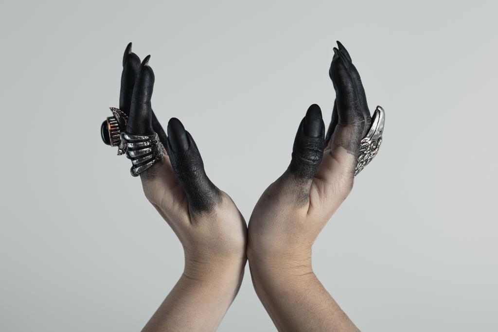 Vista recortada de manos de brujas con pintura negra y anillos de joyería sosteniendo algo aislado en gris
  - Foto, Imagen