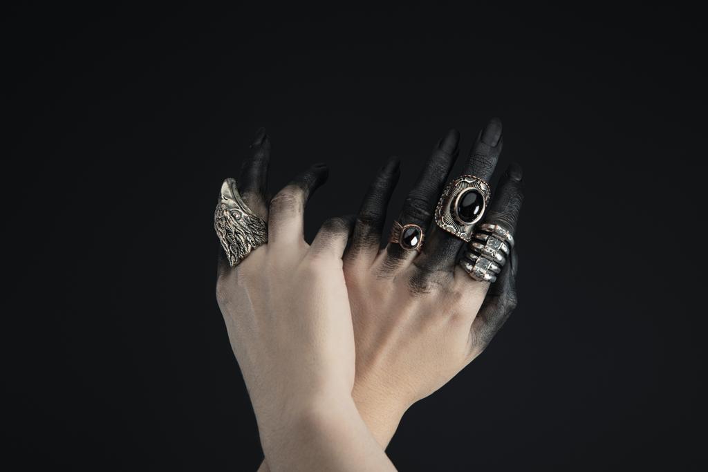 Καλλιεργημένη άποψη των χεριών μάγισσα με δαχτυλίδια κοσμήματα και μαύρη μπογιά που απομονώνονται σε μαύρο  - Φωτογραφία, εικόνα