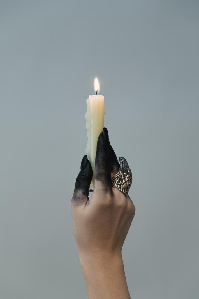 Vista recortada de bruja con tinte negro en la mano sosteniendo vela aislada en gris
 - Foto, Imagen