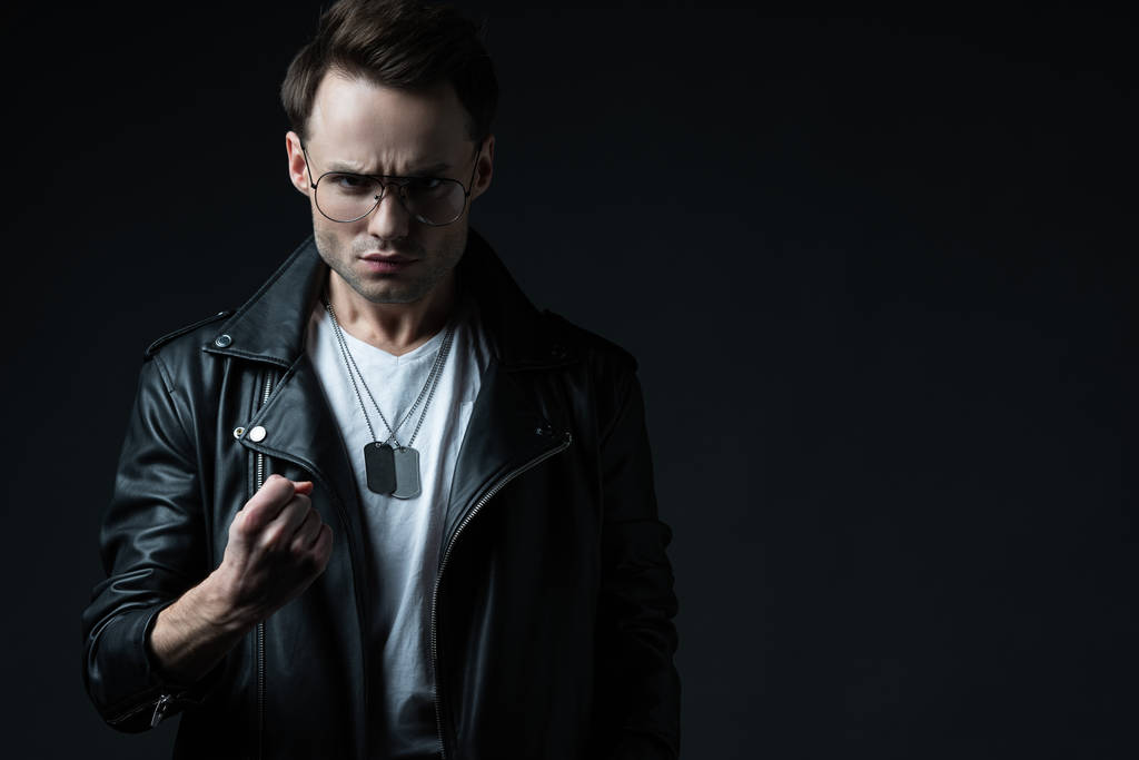 angry stylish brutal man in biker jacket showing fist isolated on black - Photo, Image
