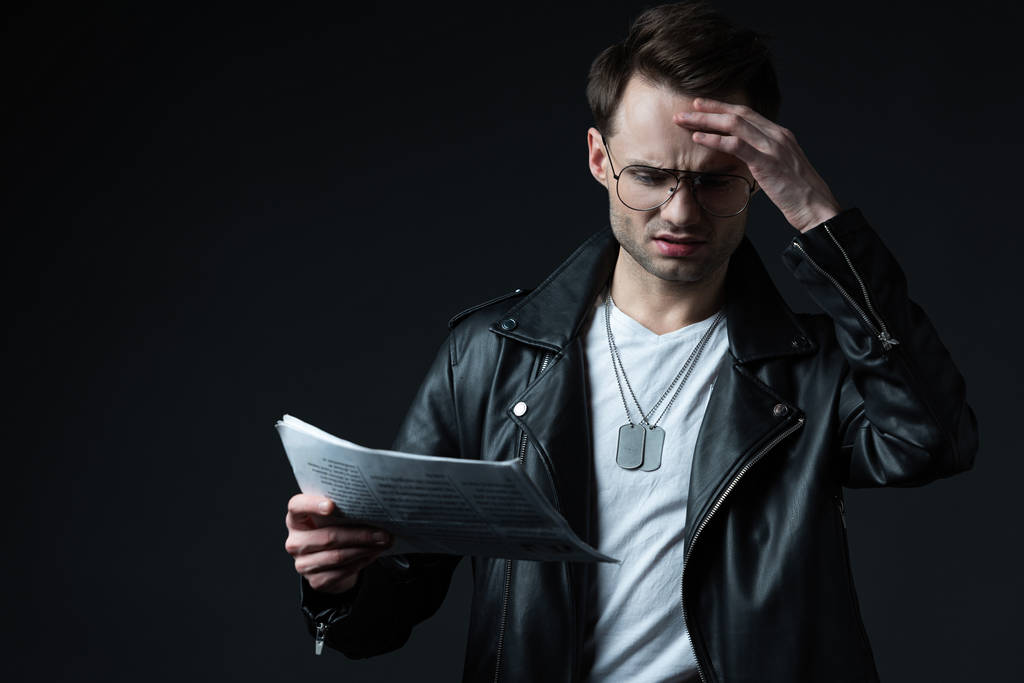 worried stylish brutal man in biker jacket with newspaper isolated on black - Photo, Image