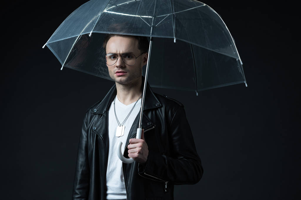preocupado hombre brutal con estilo en chaqueta de motociclista con paraguas aislado en negro
 - Foto, Imagen
