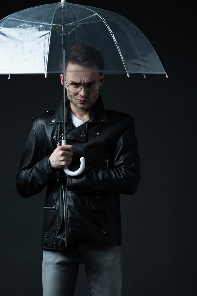 angry stylish brutal man in biker jacket with umbrella isolated on black - Photo, Image