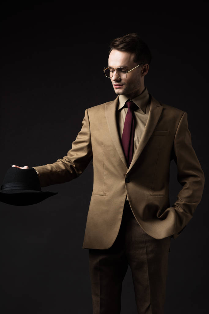 sonriente hombre elegante en traje beige y gafas con sombrero aislado en negro
 - Foto, imagen