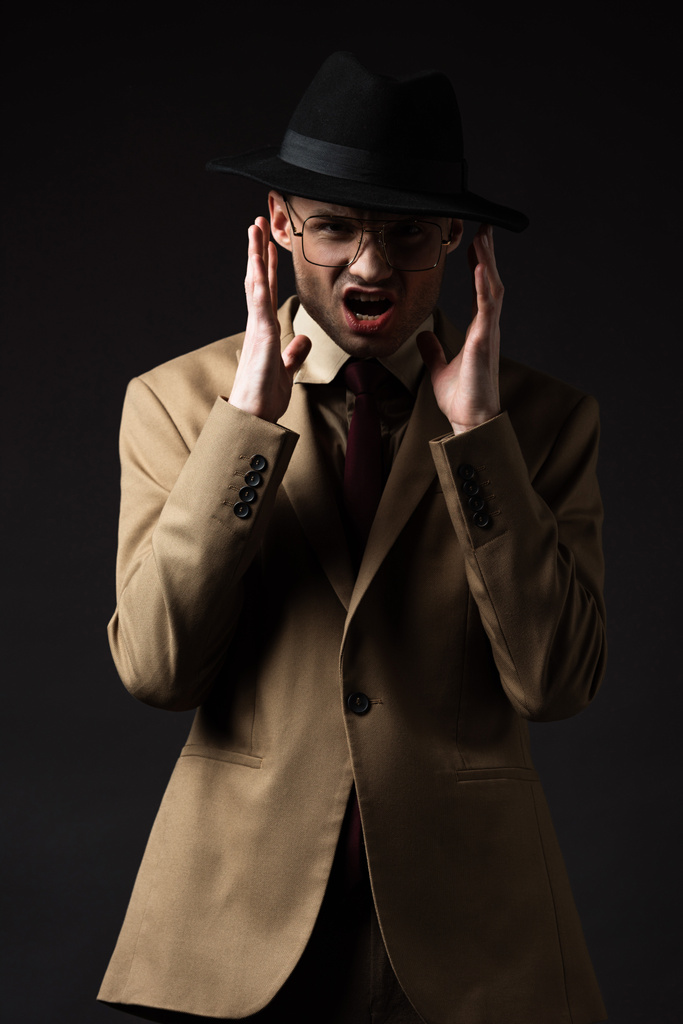 безумный элегантный мужчина в бежевом костюме, шляпе и очках, изолированных на черном
 - Фото, изображение